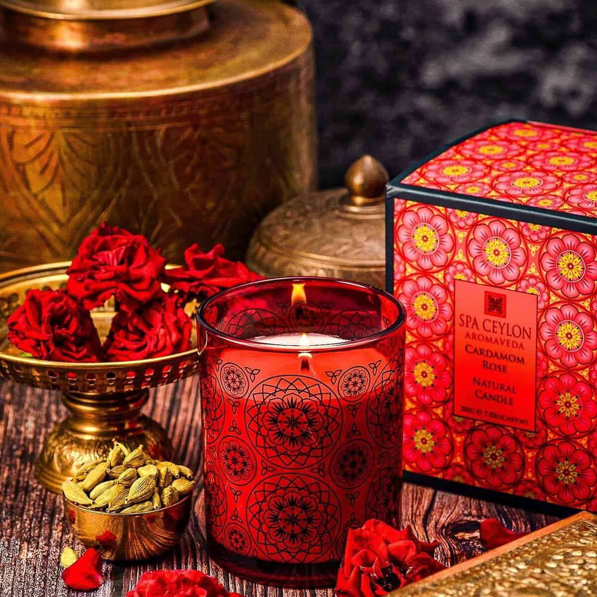 Vibrant red scented candle with intricate patterns surrounded by rose petals and spice jars, promoting luxury Spa Ceylon aromatherapy products.